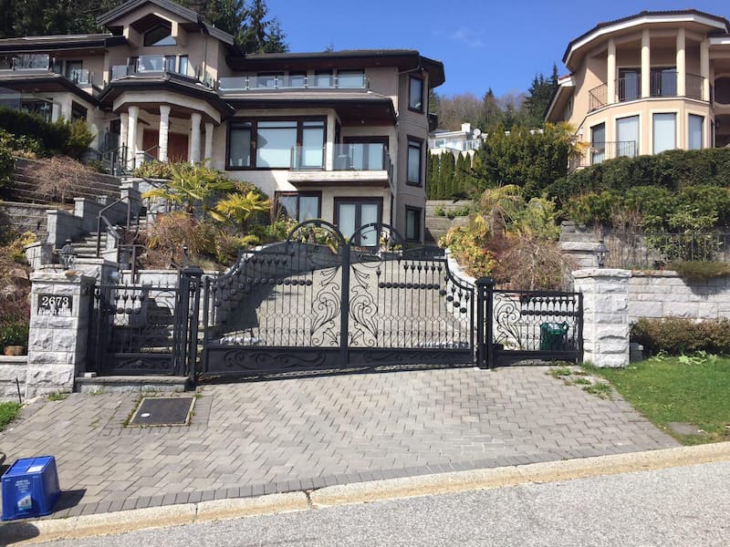 The black wrought iron gate has intricate swirls, two sections, and stone pillar supports.