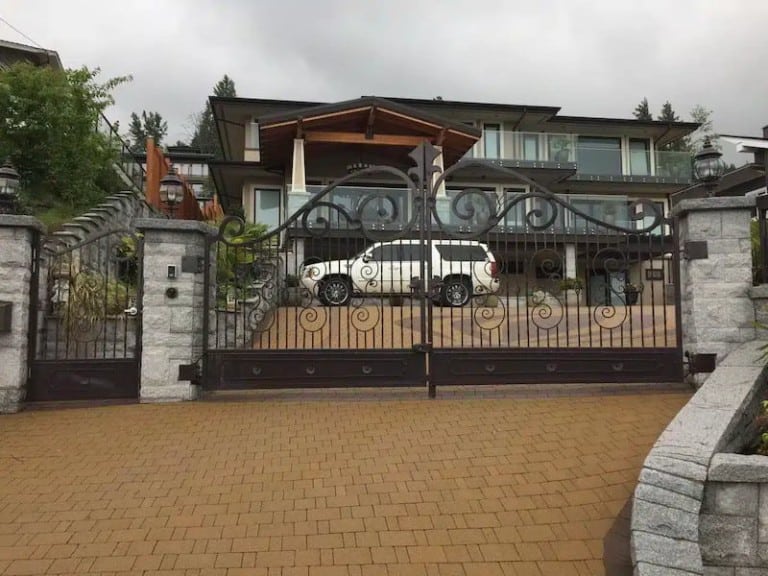 The wrought iron gate has swirls, two sections, and stone pillar supports.