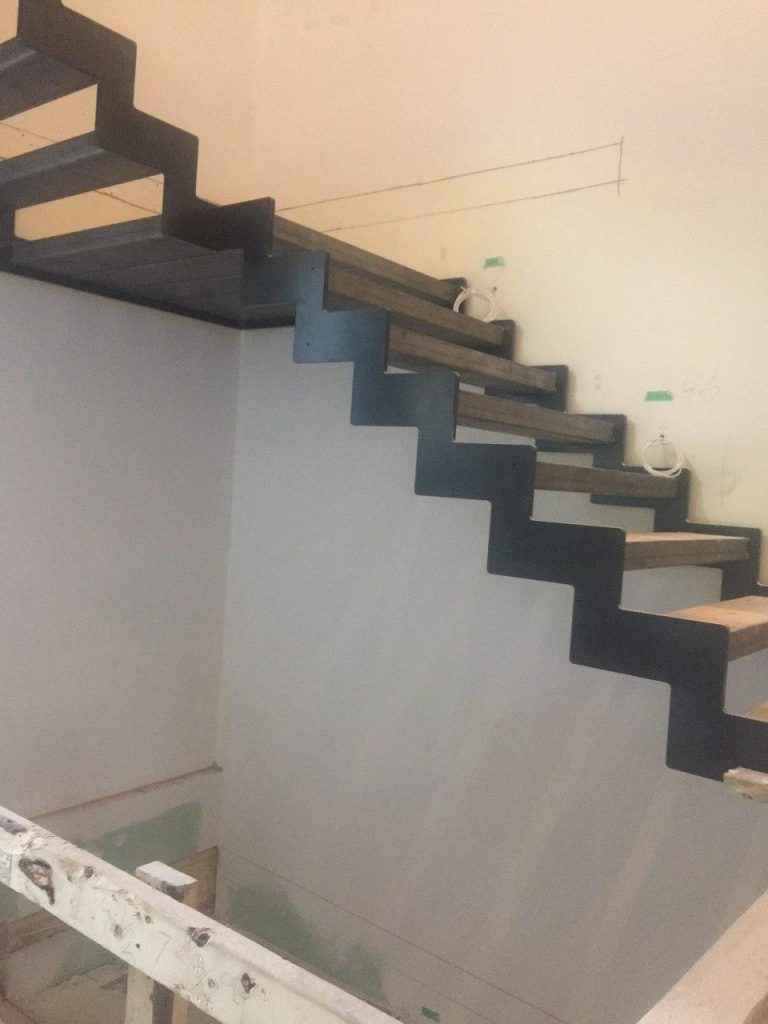 A zigzag-pattern staircase under construction, featuring a modern industrial design with exposed steel support and wooden steps.