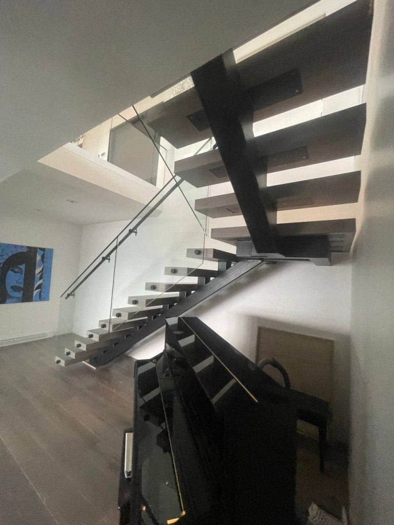 Modern floating staircase with a black metal beam, solid steps, and glass railing.