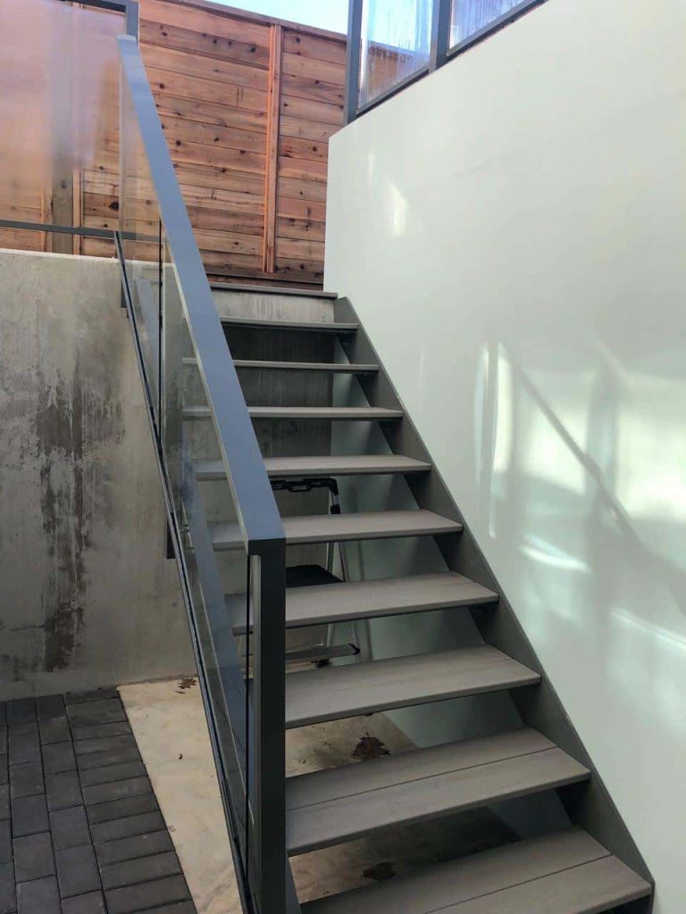 A modern staircase featuring metal framing, glass side railings, and wooden steps, creating a clean and open look.