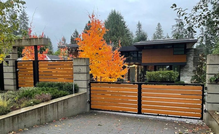 Swing driveway gate with horizontal wooden slats and a black metal frame, set between concrete pillars.