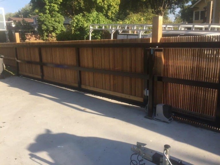 The doorway gate features wood panels with a black metal frame, operating on a sliding mechanism with motorized components.