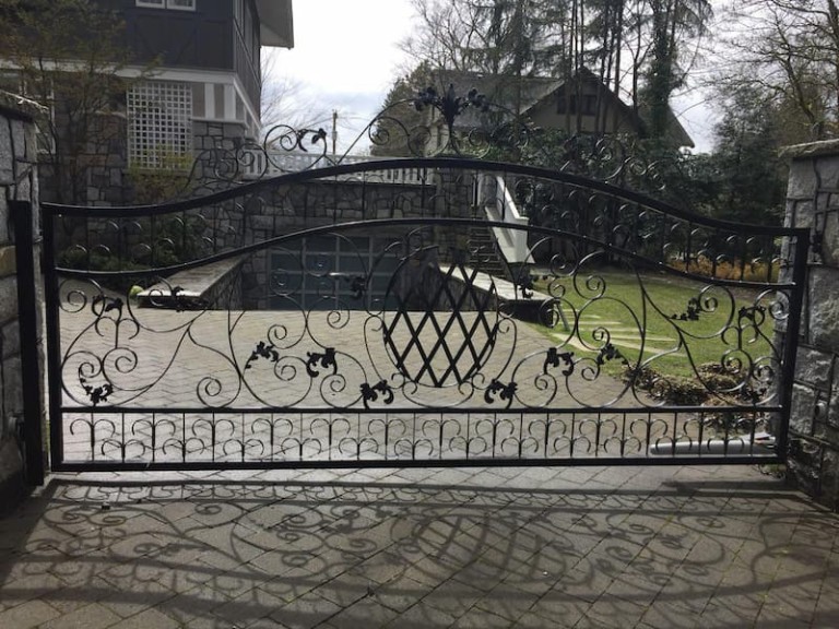 Ornate iron swing gate with intricate scrollwork and decorative lattice design, installed at a residential driveway.