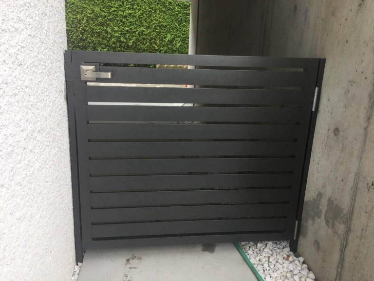 Sleek metal pedestrian gate with horizontal slats, installed in a narrow residential passageway.