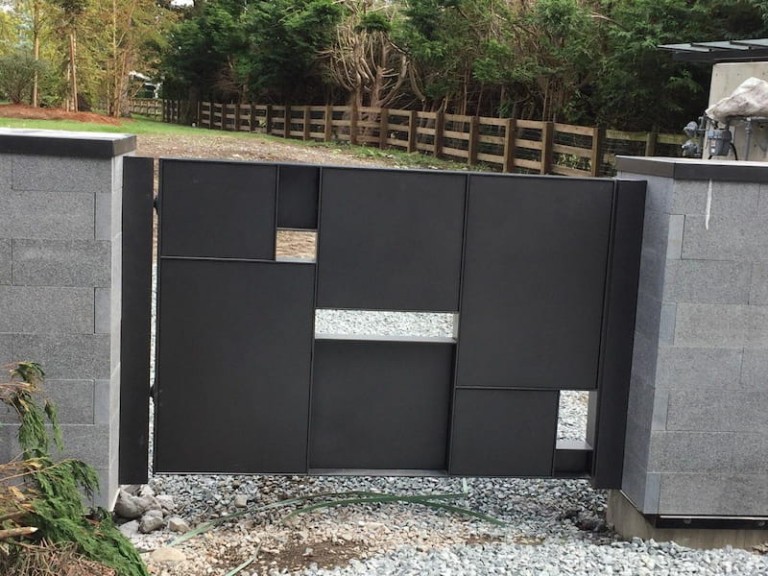 Modern metal pedestrian gate with a geometric design, featuring various cutouts, installed between two stone pillars.