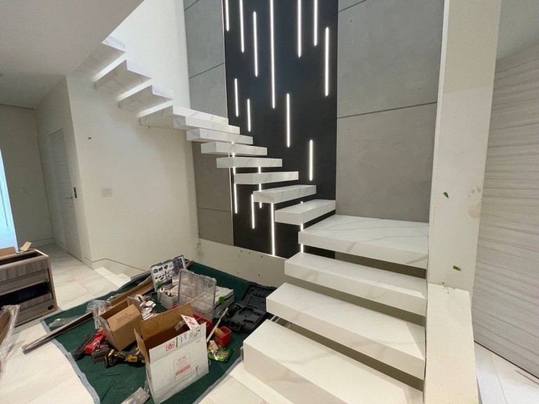 Modern floating staircase with white steps and a sleek wall featuring vertical LED lighting strips, adding a contemporary touch to the space.