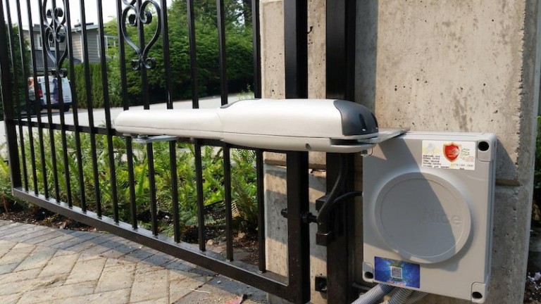 Motorized metal doorway gate with an attached actuator arm and control box for automated opening and closing.