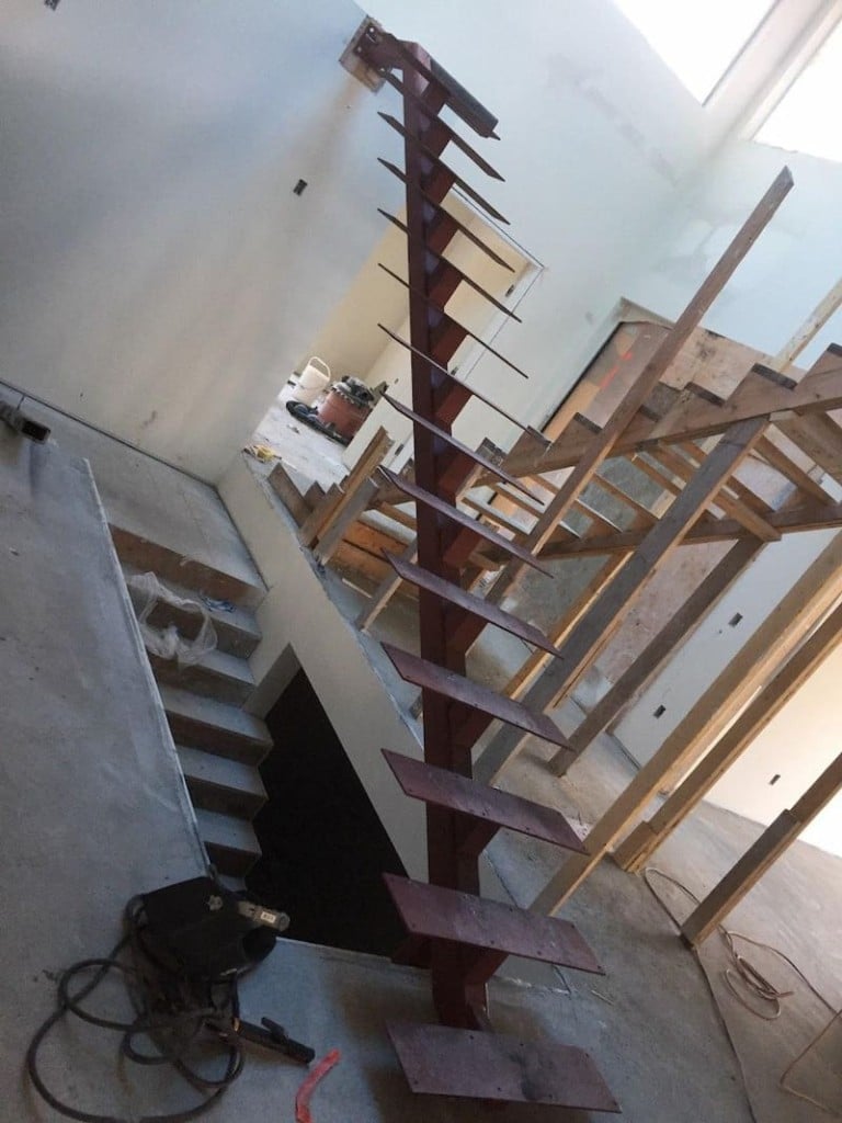 A steel staircase frame with a central beam, in the early stages of construction, with steps attached but no railing yet.