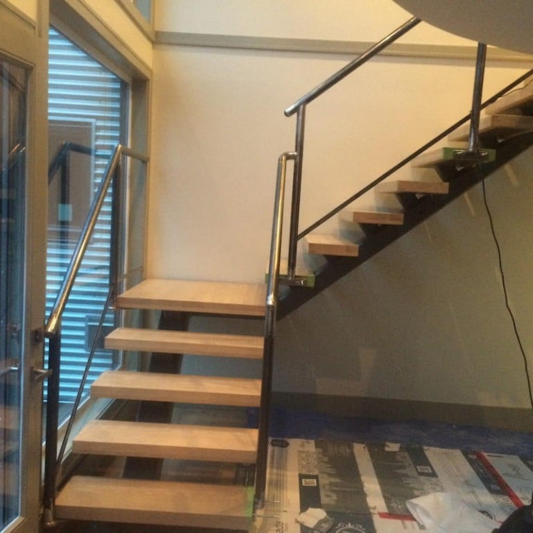 A modern staircase with wooden treads and a sleek stainless steel handrail, perfect for contemporary interiors.