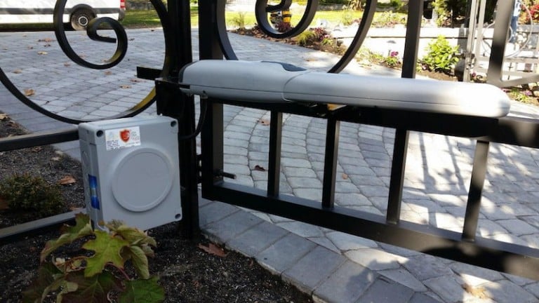 Automated metal doorway gate with decorative swirls, featuring an actuator arm and control box for motorized operation.