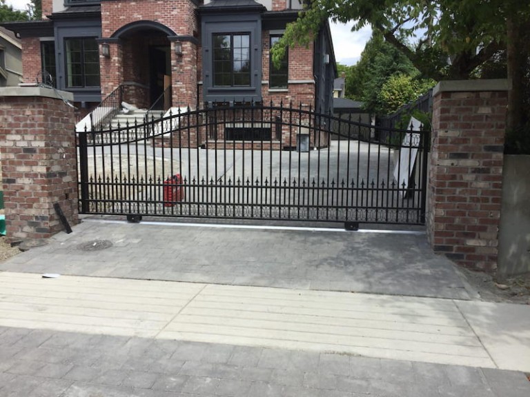 Sliding iron gate with vertical bars and pointed tops, installed at a residential driveway between brick pillars.