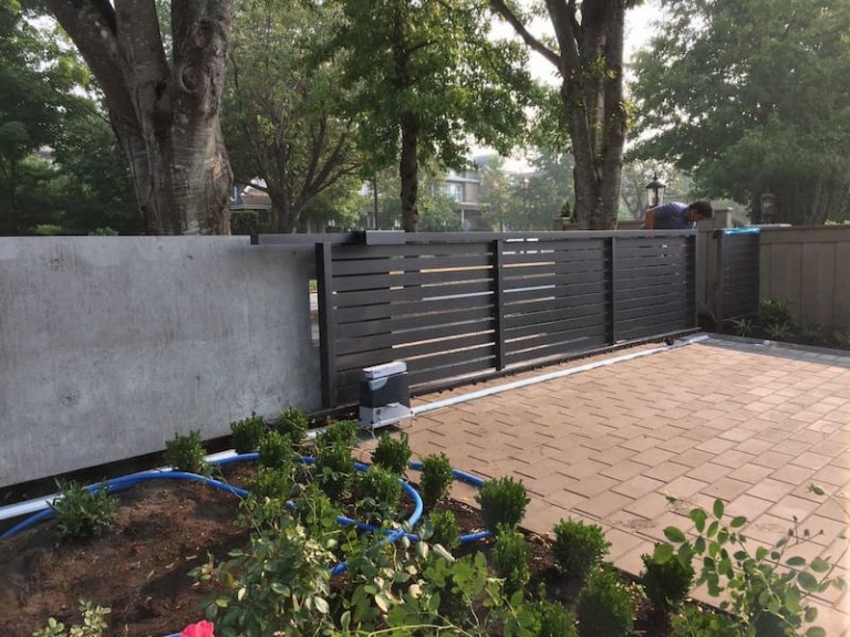 Modern sliding driveway gate with horizontal metal slats and an automated mechanism.