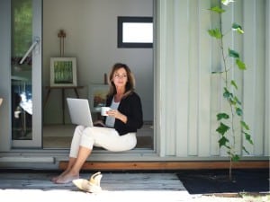 A woman sitting in a shipping container office with a laptop, enjoying the outdoors while working on her computer.