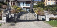 The black wrought iron gate has intricate swirls, two sections, and stone pillar supports.